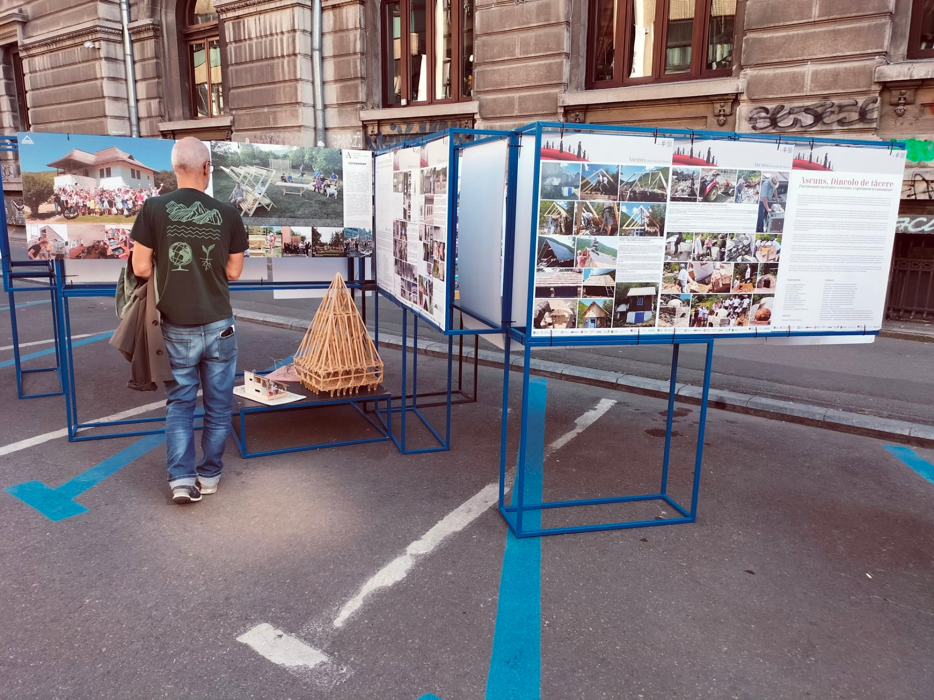 Vizitator privind panouri de expoziție și o machetă de șarpantă din lemn, amplasate în stradă